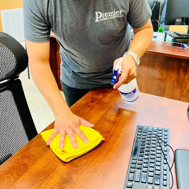 premier cleaning janitorial employee wiping desk yellow rag spray bottle